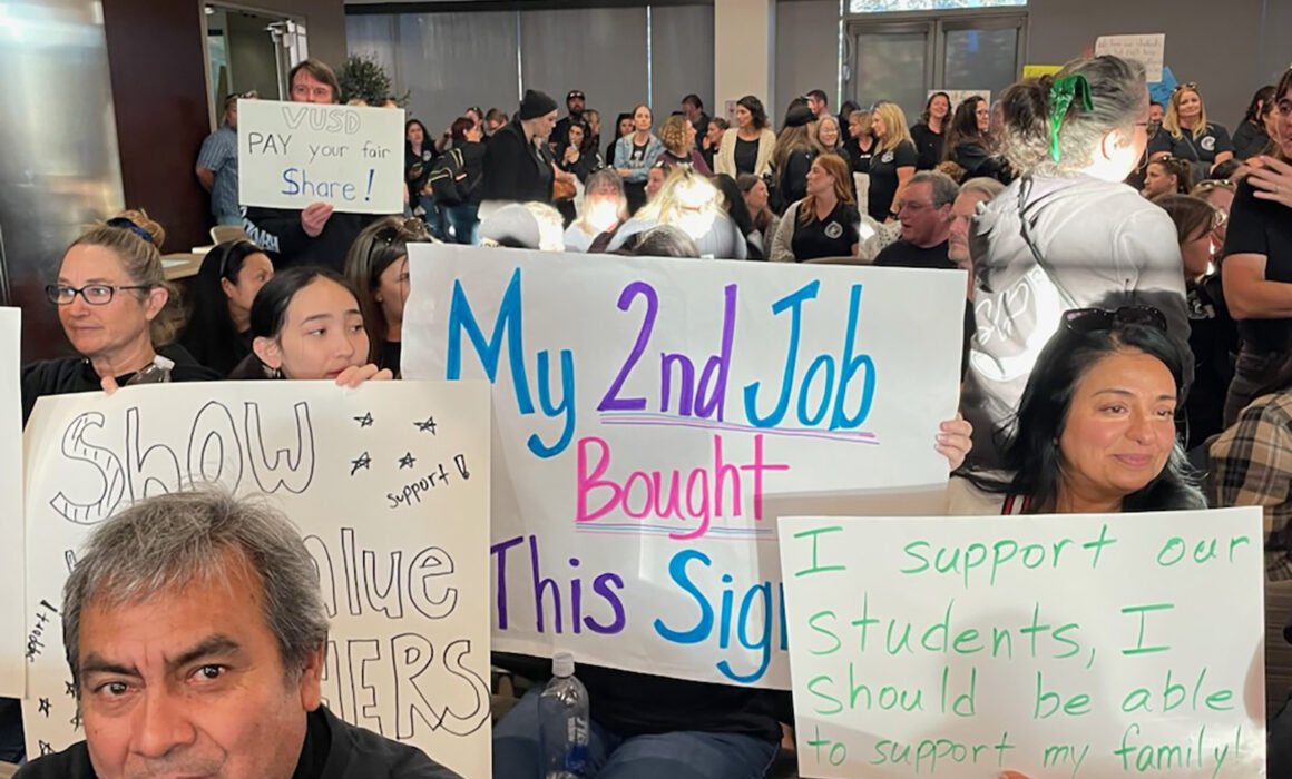 A crowd of people holding up signs that with messages of support for teachers and students.